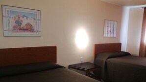 A hotel room with two single beds, a nightstand, a wall-mounted lamp, and a framed picture. - Star Motel (Morden)