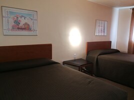 Habitación de hotel con dos camas individuales, una mesita de noche, una lámpara de pared y un cuadro enmarcado.