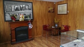 A room with a fireplace, wooden paneling, a framed picture, a glass display case, and two red chairs. - Star Motel (Morden)