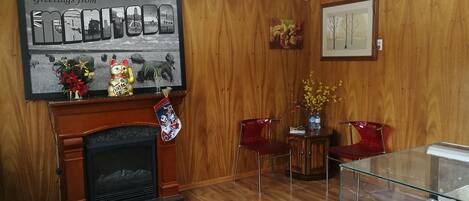 A room with a fireplace, wooden paneling, a framed picture, a glass display case, and two red chairs.