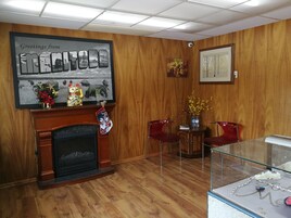 Una habitación con chimenea, paneles de madera, un cuadro enmarcado, una vitrina de vidrio y dos sillas rojas.