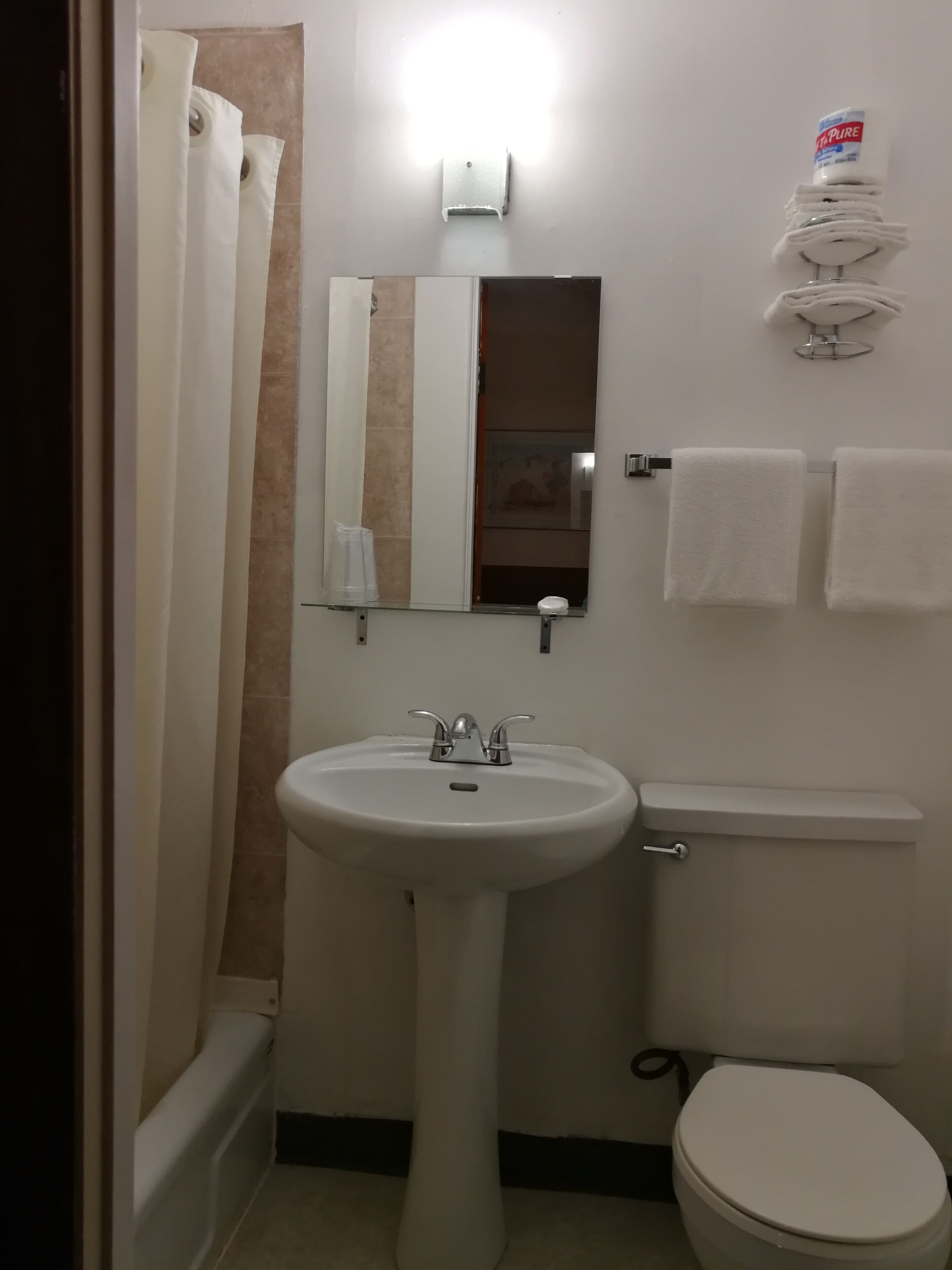 Un baño con lavamanos blanco, inodoro, cortina de ducha, espejo y toallero.