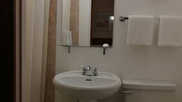 Un baño con lavamanos blanco, inodoro, cortina de ducha, espejo y toallero.