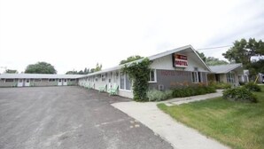 A motel with a row of single-story buildings, a parking lot, and a grassy area with a sidewalk. - Star Motel (Morden)