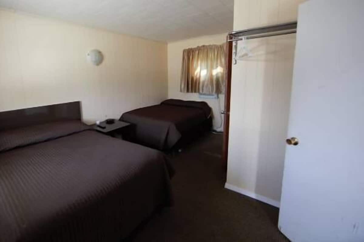 Une chambre d’hôtel avec deux lits, une table de chevet, une armoire et une lampe fixée au mur.