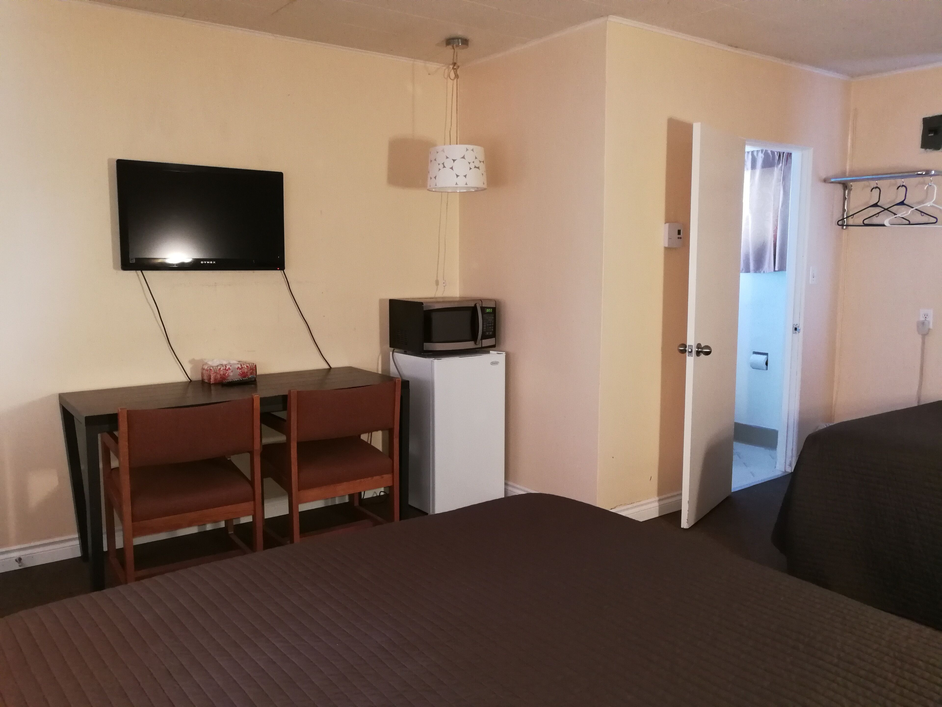 A hotel room with a bed, a desk with a chair, a television, a microwave, and a door leading to a bathroom.