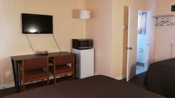 A hotel room with a bed, a desk with a chair, a television, a microwave, and a door leading to a bathroom.