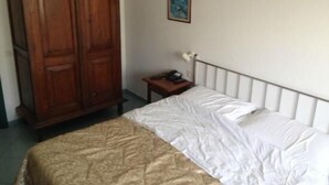 Een slaapkamer met een bed, een houten garderobe, een klein nachtkastje en een wandlamp.