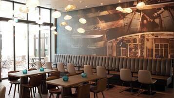 Un restaurante con mesas altas y cabinas, iluminación colgante y un mural de barcos en la pared.