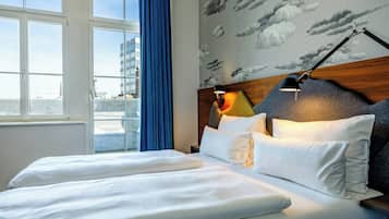 A hotel room with a bed, a nightstand, a lamp, a window with curtains, and a city view.