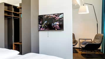 A hotel room with a bed, a TV mounted on the wall, a desk, a chair, and a wardrobe.
