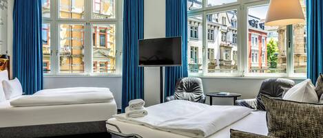 Habitación de hotel con dos camas, un televisor, una mesita y vistas a edificios históricos.