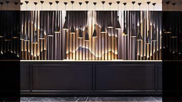 Zona de recepción de diseño moderno, con un mostrador oscuro, luminarias verticales y un panel de pared texturizado.