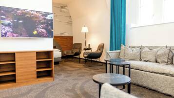 Una habitación de hotel moderna con televisión de pantalla plana, un sofá, dos sillones, una mesita de centro y una lámpara.