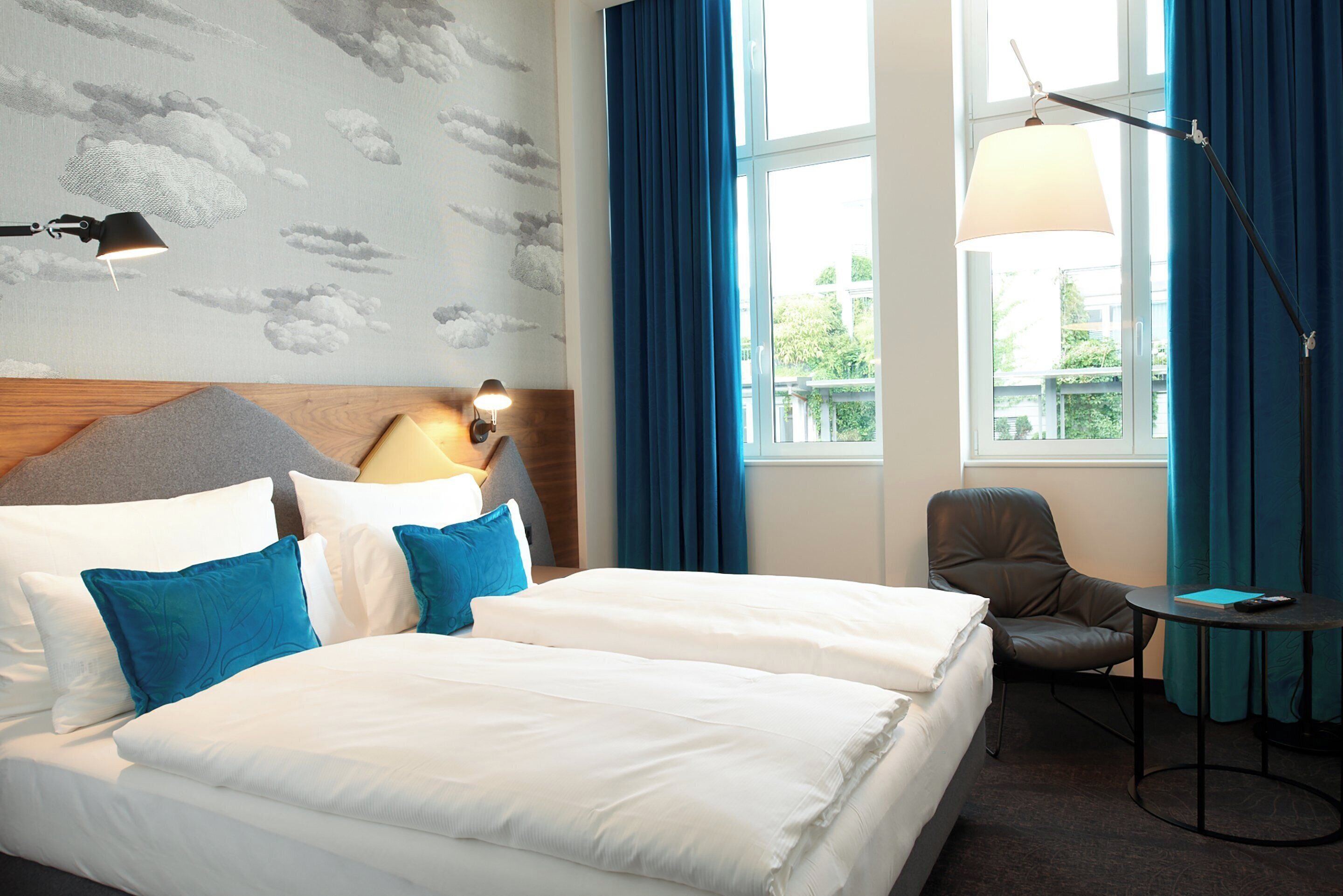 A hotel room with a large bed, a desk, a chair, a lamp, and a view of the outdoors.