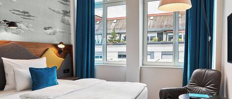A hotel room with a large bed, a desk, a chair, and a window with curtains.