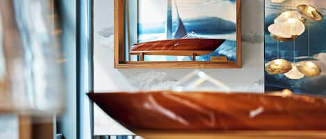 A framed picture of a sailboat, a wooden bowl, and hanging light fixtures.