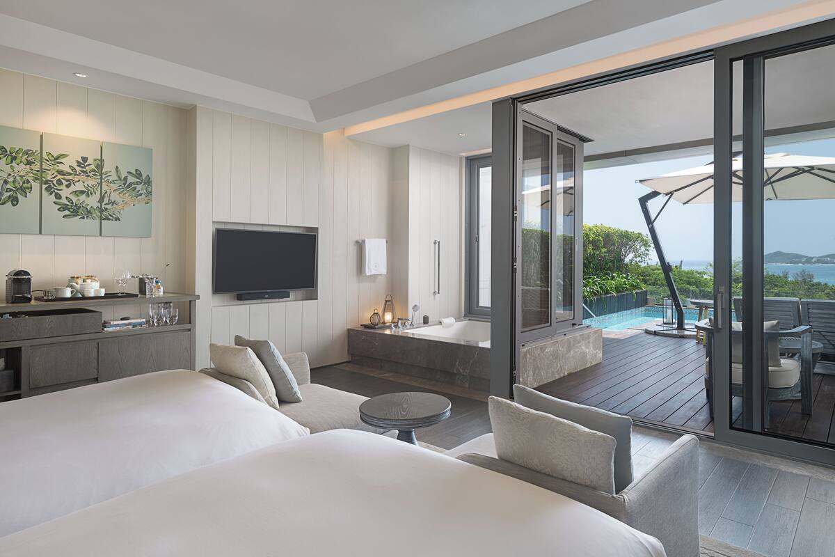 Una habitación de hotel moderna con una cama grande, una zona de estar, una cocina y un balcón con vistas al mar.