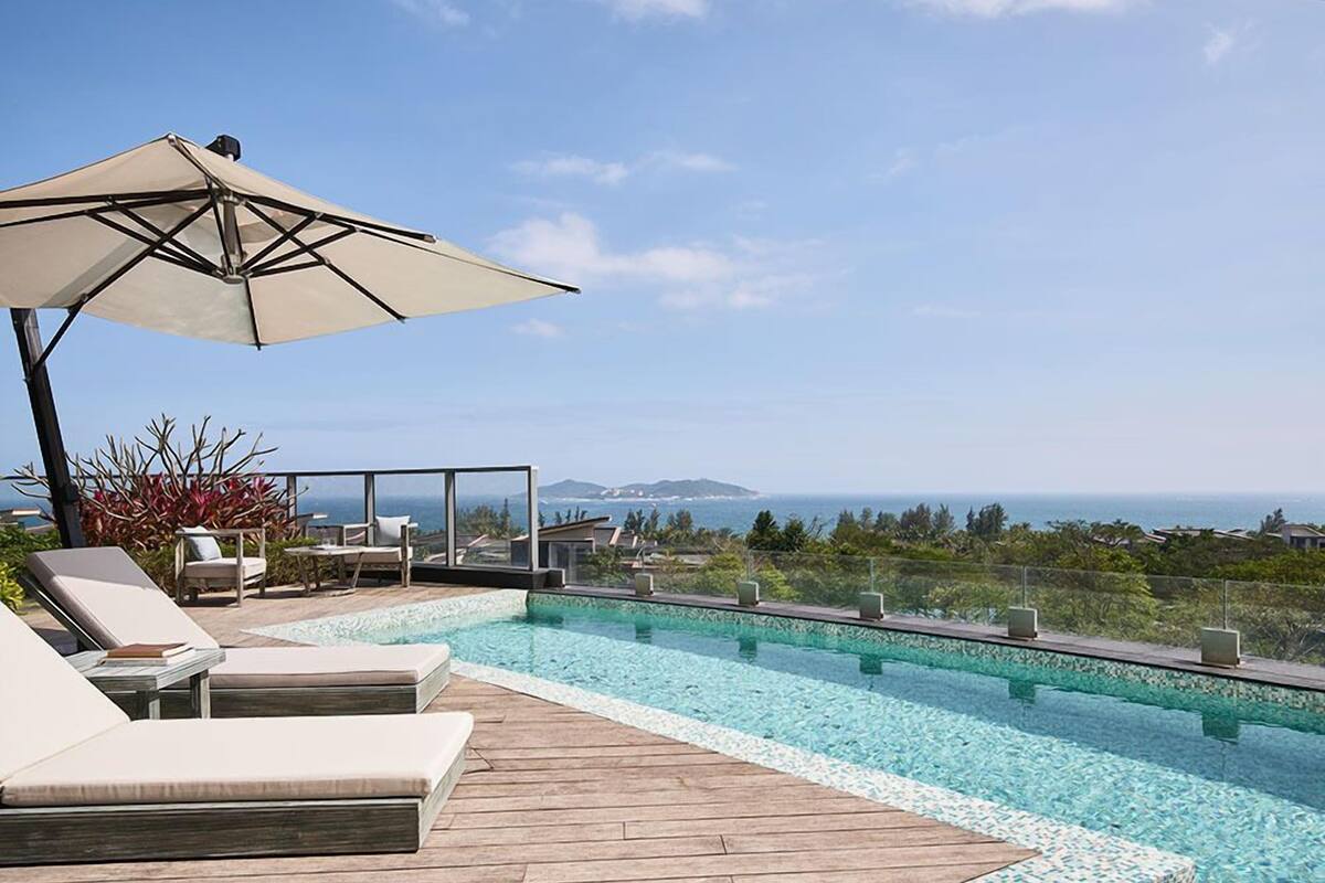 Zona junto a la piscina con sillones de descanso y una sombrilla, con vista despejada al océano.