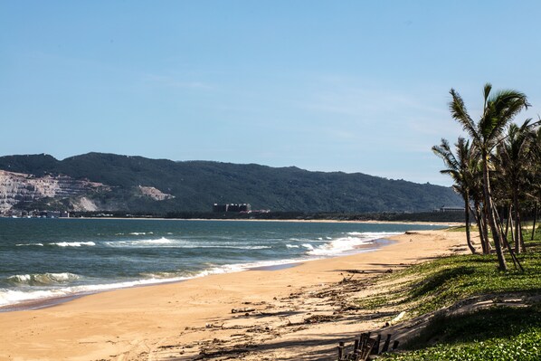 Una playa con aguas cristalinas, una orilla arenosa y un promontorio boscoso al fondo.