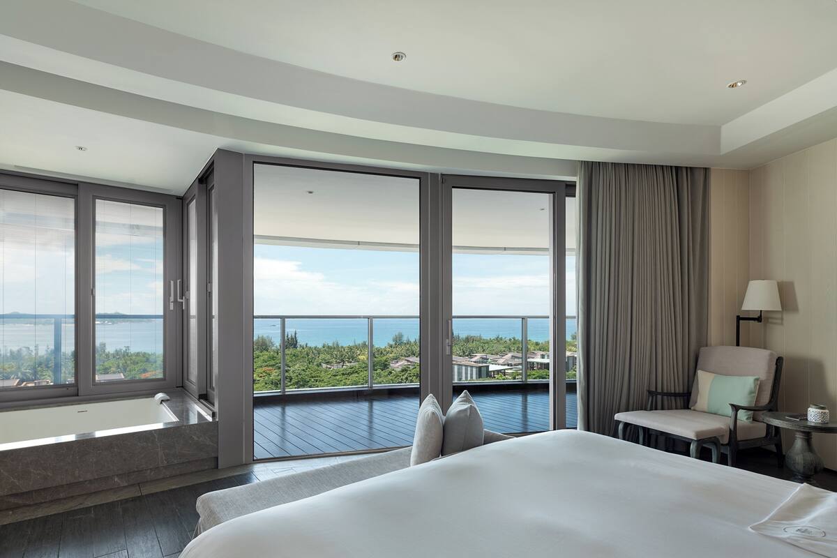 Habitación de hotel con una cama grande, vistas al mar, un balcón con vistas y una silla junto a la ventana.
