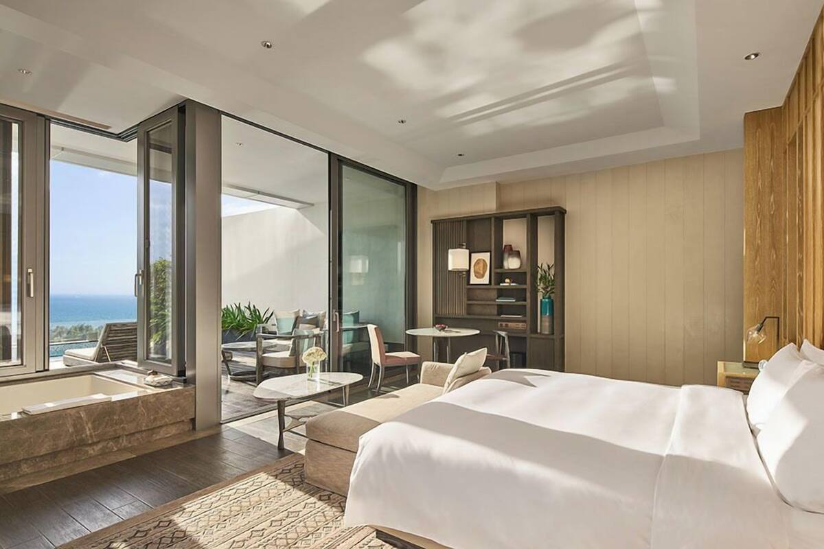 Una habitación de hotel moderna con una cama grande, un balcón con asientos y vista al océano.