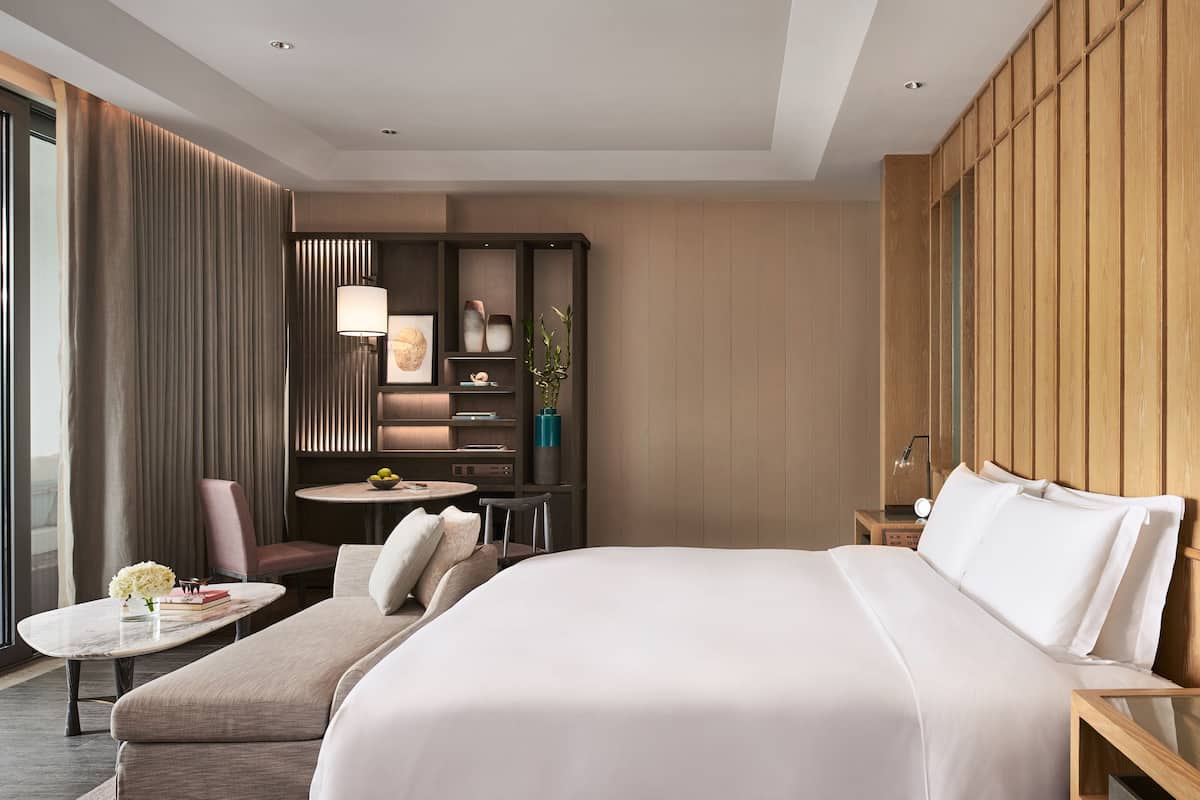 Habitación de hotel moderna con una cama grande, una zona de estar con una mesa, un escritorio con lámpara y vistas por la ventana.