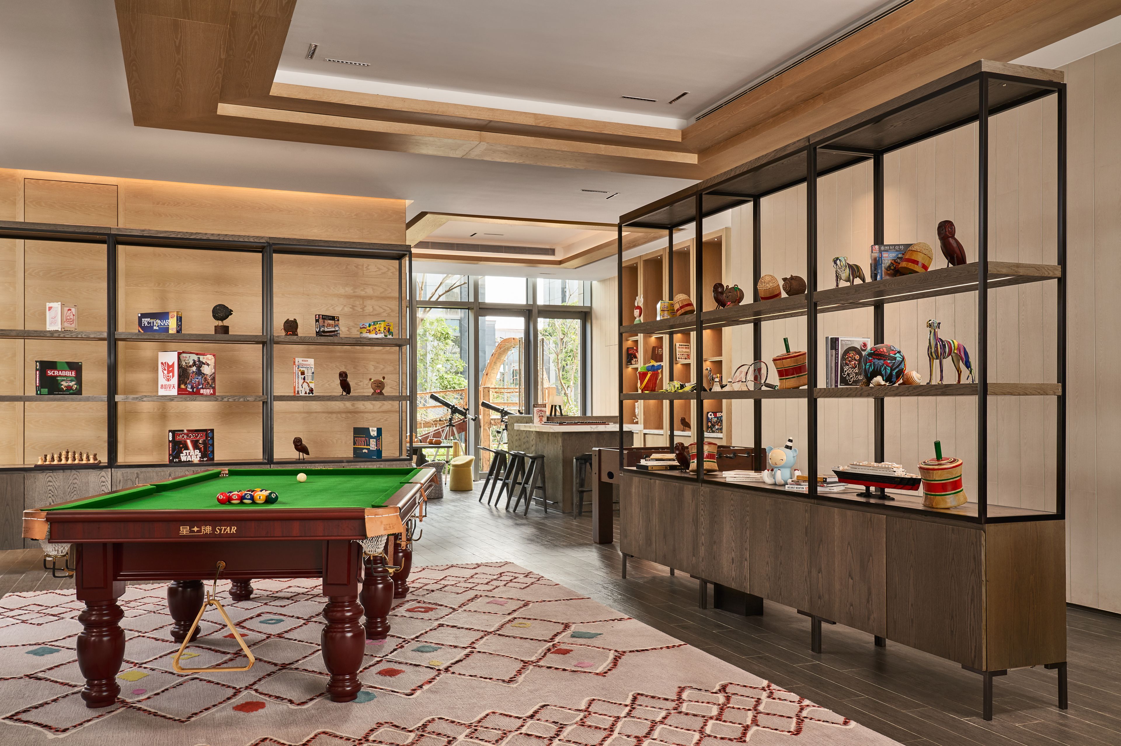 A modern indoor space with a pool table, shelves with various items, and a view to the outdoors.