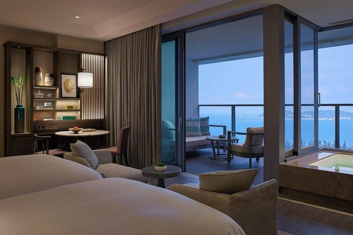 Habitación de hotel con una cama grande, un escritorio y un balcón con vista al mar.