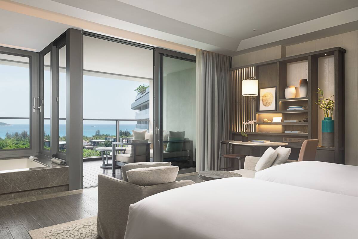 Una habitación de hotel moderna con una cama grande, un escritorio y un balcón con vistas al océano.
