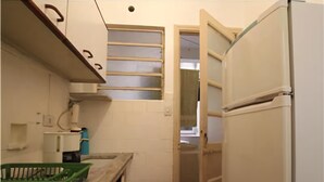 Une cuisine de taille réduite avec des meubles blancs, un réfrigérateur et un plan de travail sur lequel se trouve un panier vert.