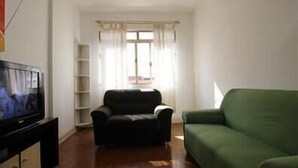 Un salon avec un téléviseur, un canapé vert, un fauteuil noir et une fenêtre avec des rideaux.