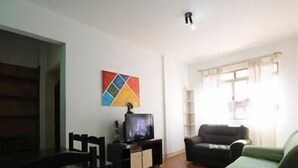 Un salon comprenant un téléviseur, un canapé, une table à manger et une œuvre d’art colorée accrochée au mur.