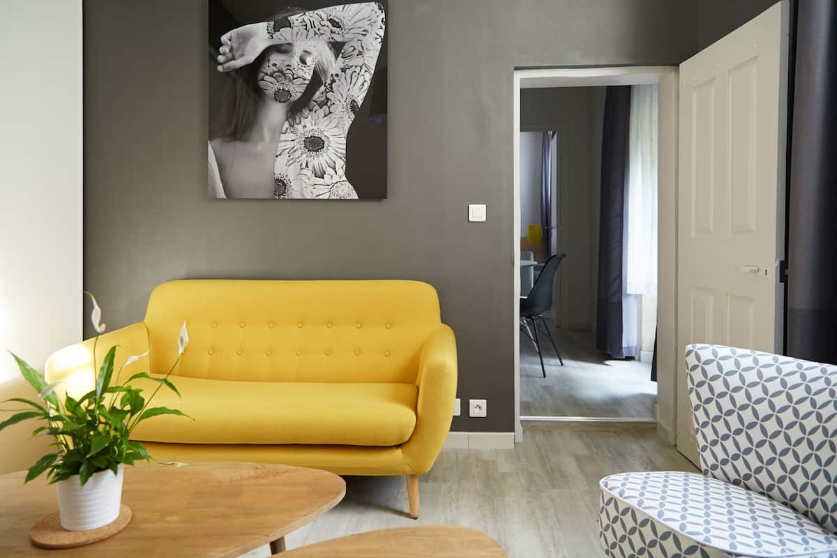 A modern living room with a yellow sofa, a patterned armchair, and a large abstract painting on the wall.