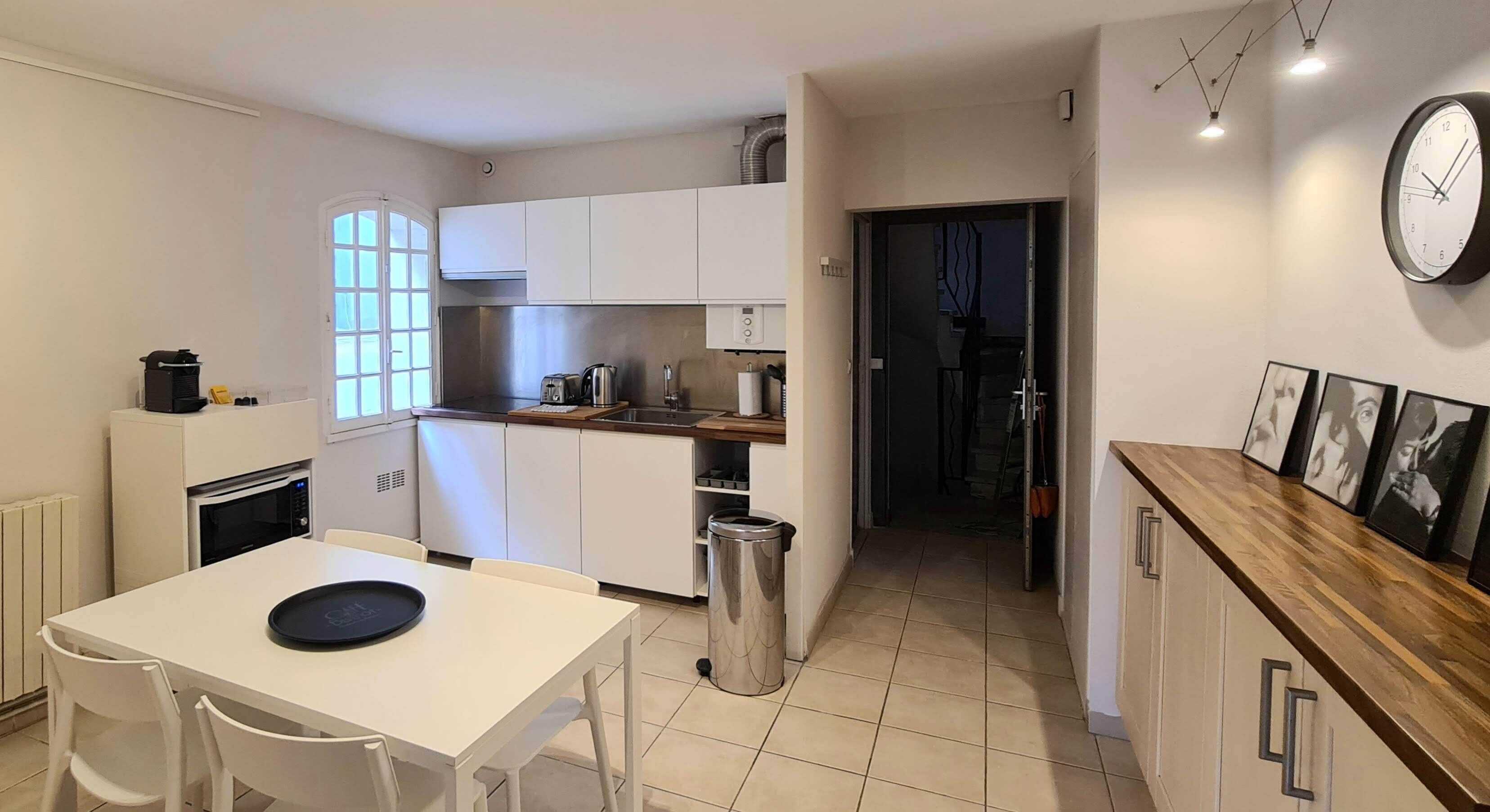 Cocina compacta con armarios blancos, microondas, lavamanos y zona de comedor con mesa y sillas.