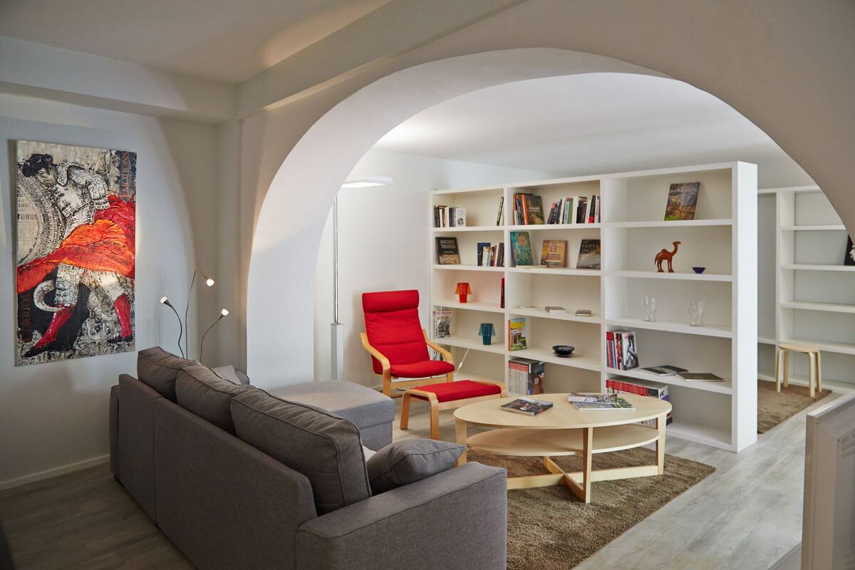 A modern living room with a sofa, a red armchair, a coffee table, and a bookshelf filled with books and decorative items.