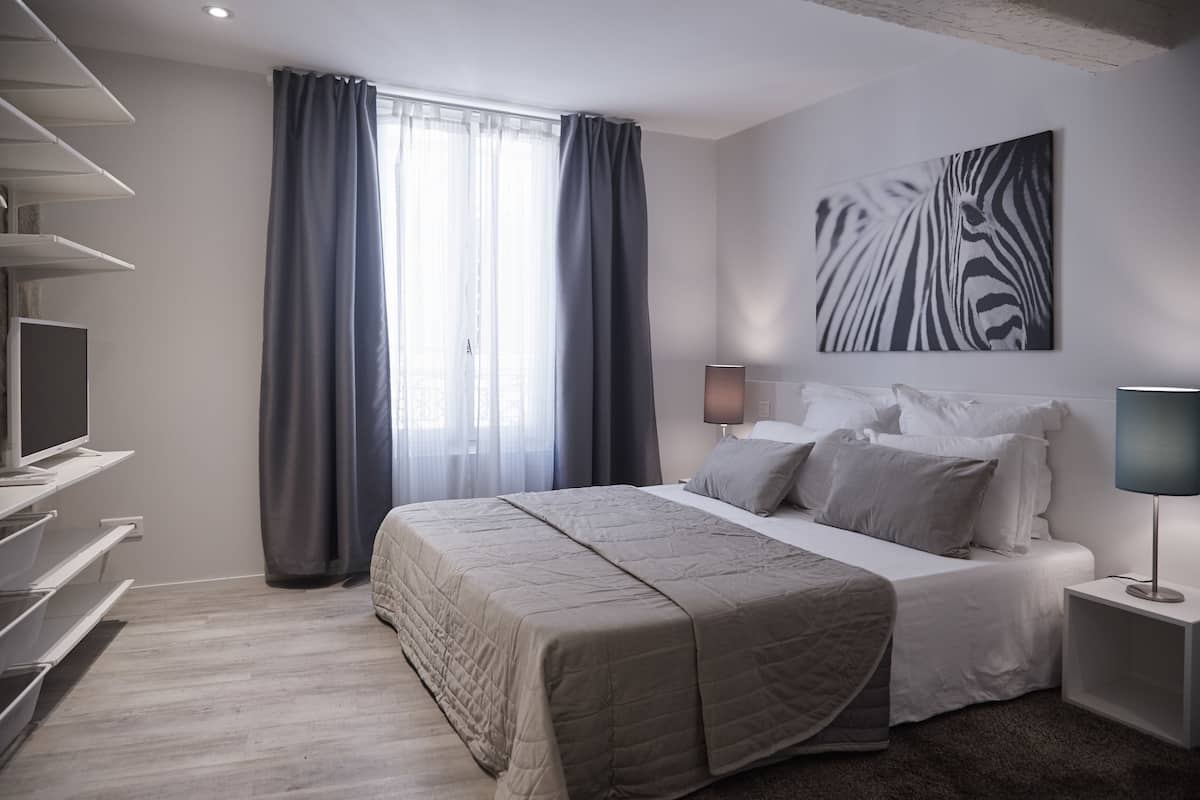 A modern bedroom with a large bed, a TV on a shelf, a zebra artwork on the wall, and a window with curtains.