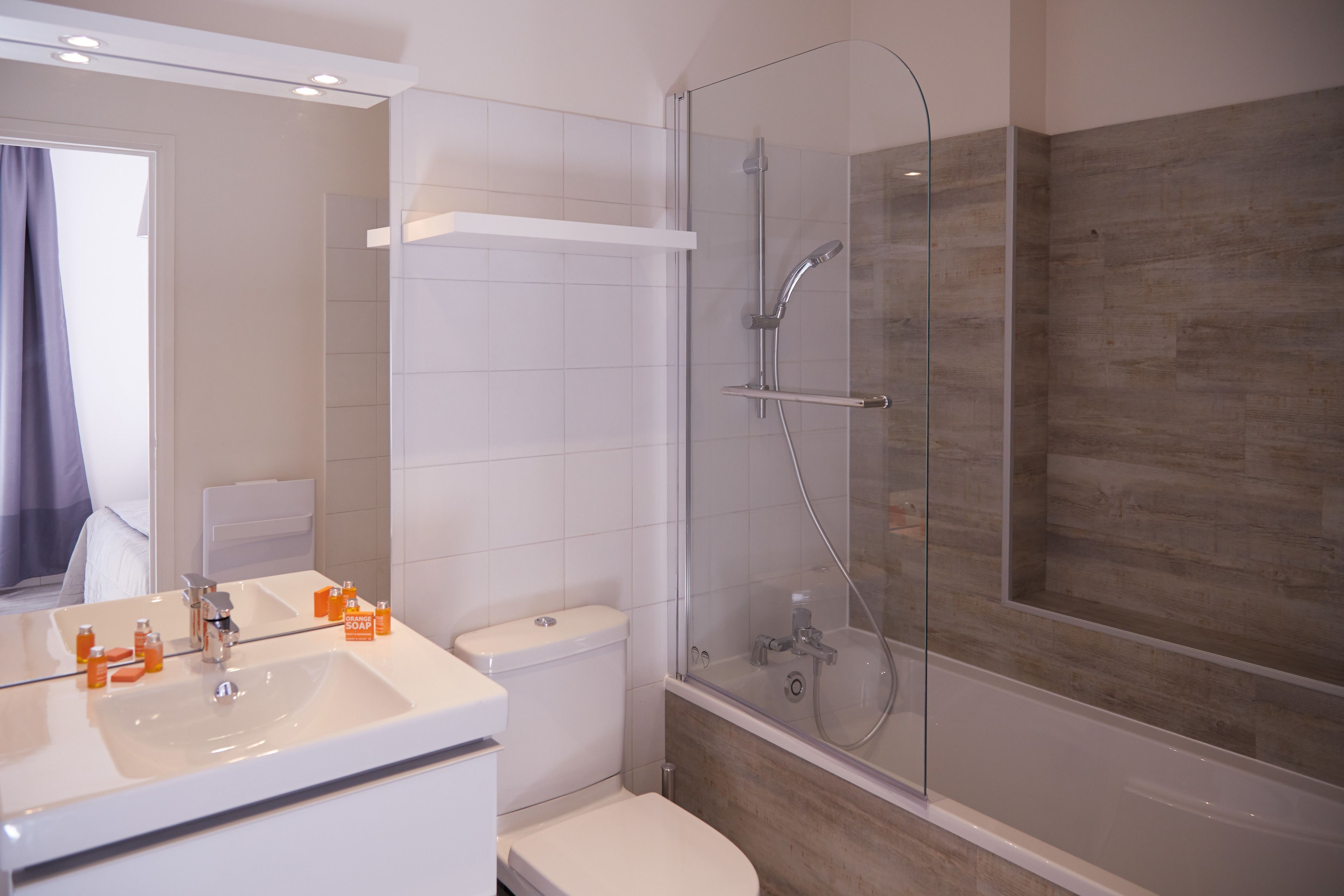A modern bathroom with a glass-enclosed shower, a white sink with soap dispensers, and a toilet.
