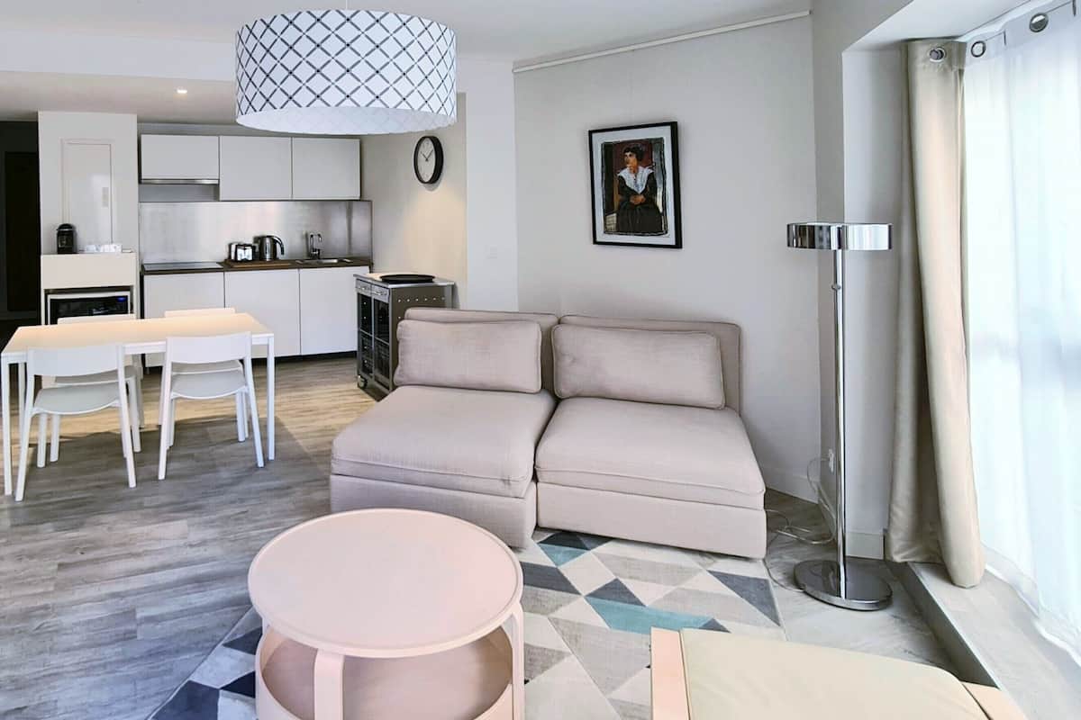 A modern living room with a sofa, a dining table with chairs, a kitchen area, and artwork on the walls.