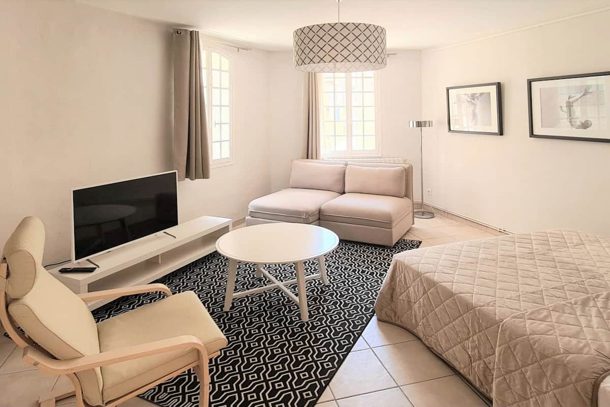A modern hotel room with a large bed, a sofa, a TV, a small table, and artwork on the walls.