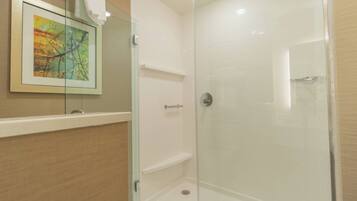A glass-enclosed shower with a white tiled wall, a framed picture, and a towel hanging on the door.