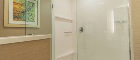 A glass-enclosed shower with a white tiled wall, a framed picture, and a towel hanging on the door.