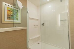 A glass-enclosed shower with a white tiled wall, a framed picture, and a towel hanging on the door.
