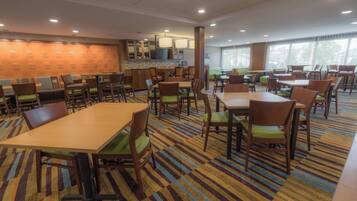 A hotel dining area with multiple tables and chairs, a bar area, and a patterned carpet.
