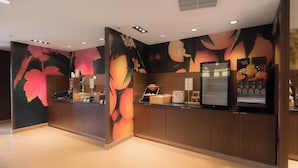 A reception area with a wooden counter, a fruit juice dispenser, and a wall mural with floral designs. - Fairfield Inn & Suites by Marriott Gaylord (Gaylord)