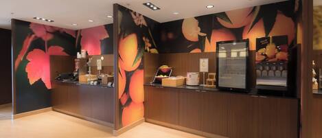 A reception area with a wooden counter, a fruit juice dispenser, and a wall mural with floral designs.