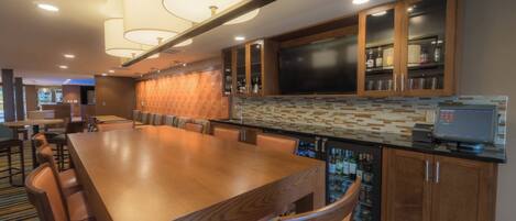 A spacious dining area with a long wooden table and comfortable chairs, a modern kitchen with a tiled backsplash, and a bar area with a cash register.