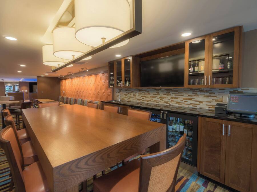 A spacious dining area with a long wooden table and comfortable chairs, a modern kitchen with a tiled backsplash, and a bar area with a cash register.