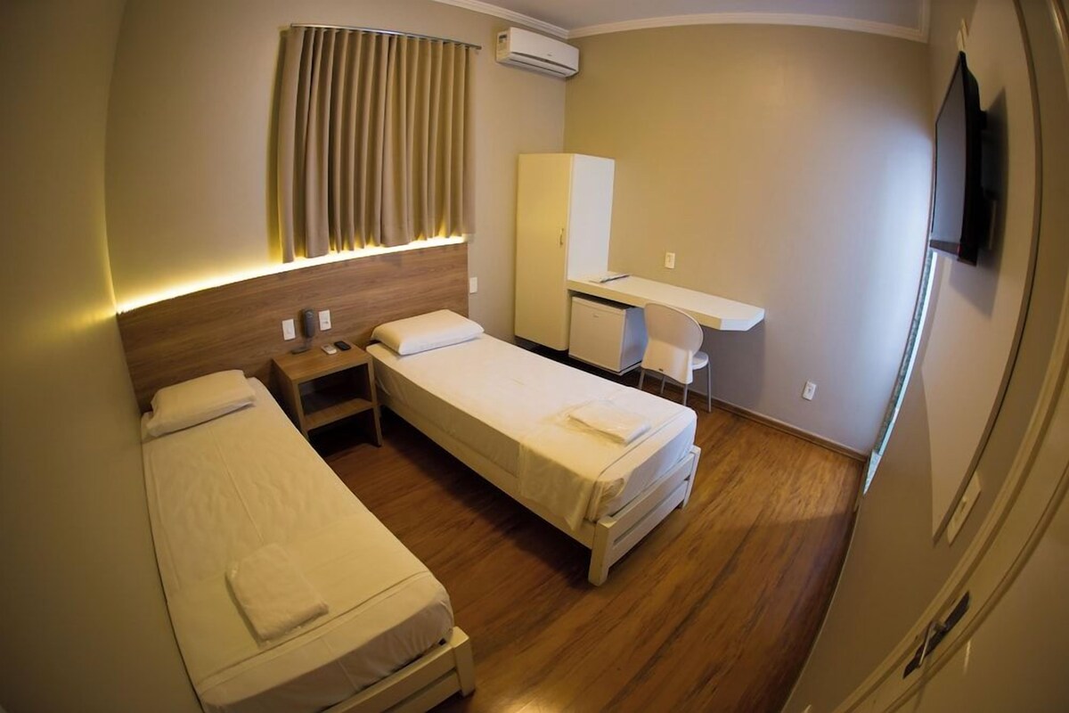 Een hotelkamer met twee eenpersoonsbedden, een bureau, een kledingkast en een airconditioning.