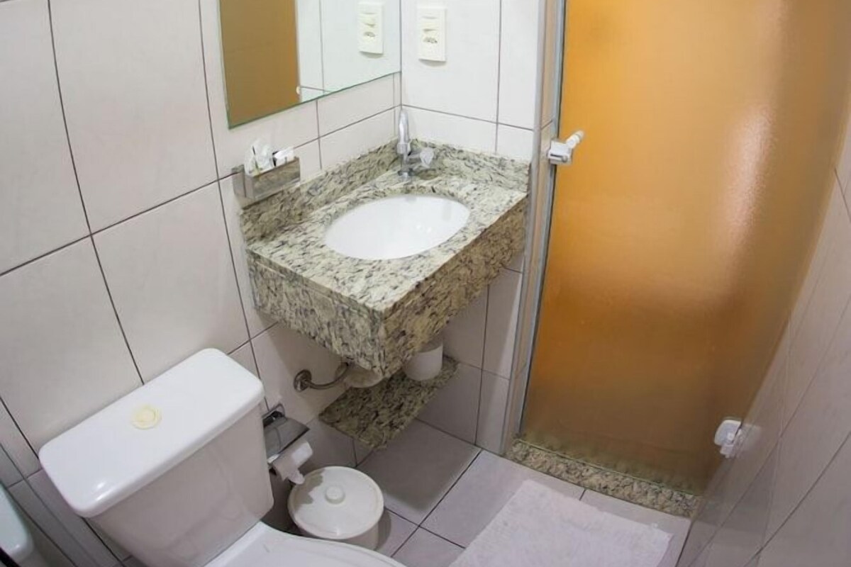 Un baño con inodoro blanco, lavamanos de granito, espejo y zona de ducha.
